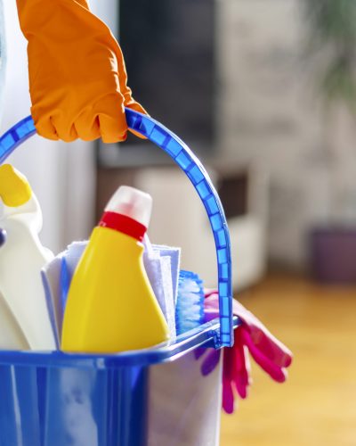 Woman in rubber gloves with bucket of cleaning supplies ready to clean up her apartment. Housewife has many household chores, domestic work and professional cleaning service. Low depth of field